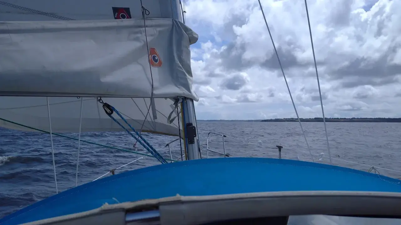 Vue depuis un voilier, le **lofer voile** blanc gonflé par le vent, sur une mer agitée sous un ciel nuageux.