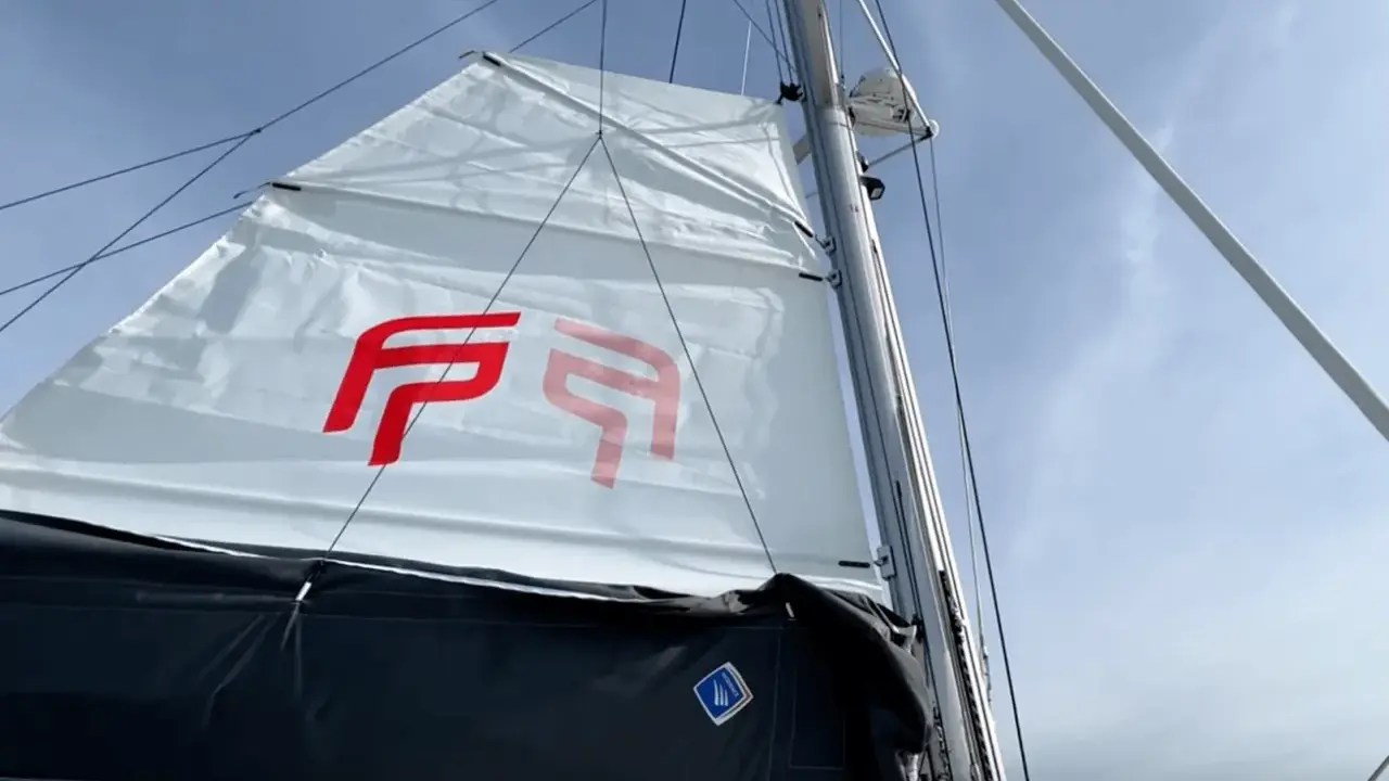 Voile blanche avec logo rouge, prête à naviguer à la voile sous un ciel bleu.