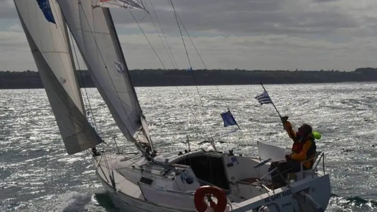 Voilier naviguant par gros temps, le skipper tient un drapeau. La fiche technique du premier 260 est visible sur la coque.