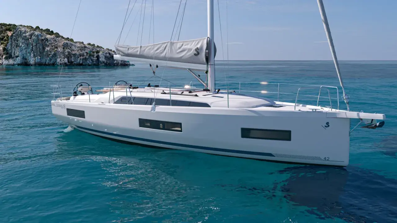 Un voilier blanc moderne navigue sur des eaux turquoise claires, près d'une île rocheuse. Ce modèle, le "Oceanis 42", pourrait bien être le meilleur voilier habitable pour vos aventures.
