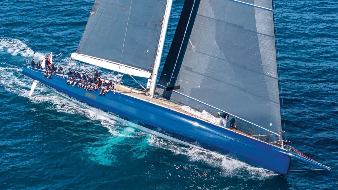 Un grand voilier bleu glisse sur l'eau, tel un tapis volant bateau. L'équipage est à bord, profitant de la navigation.