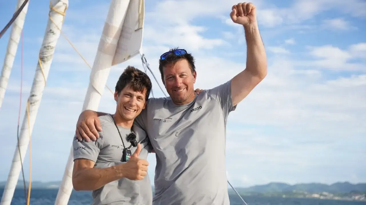 Guillaume Pirouelle et son coéquipier célèbrent une victoire sur l'eau, bras levés et souriants, sous un ciel bleu.