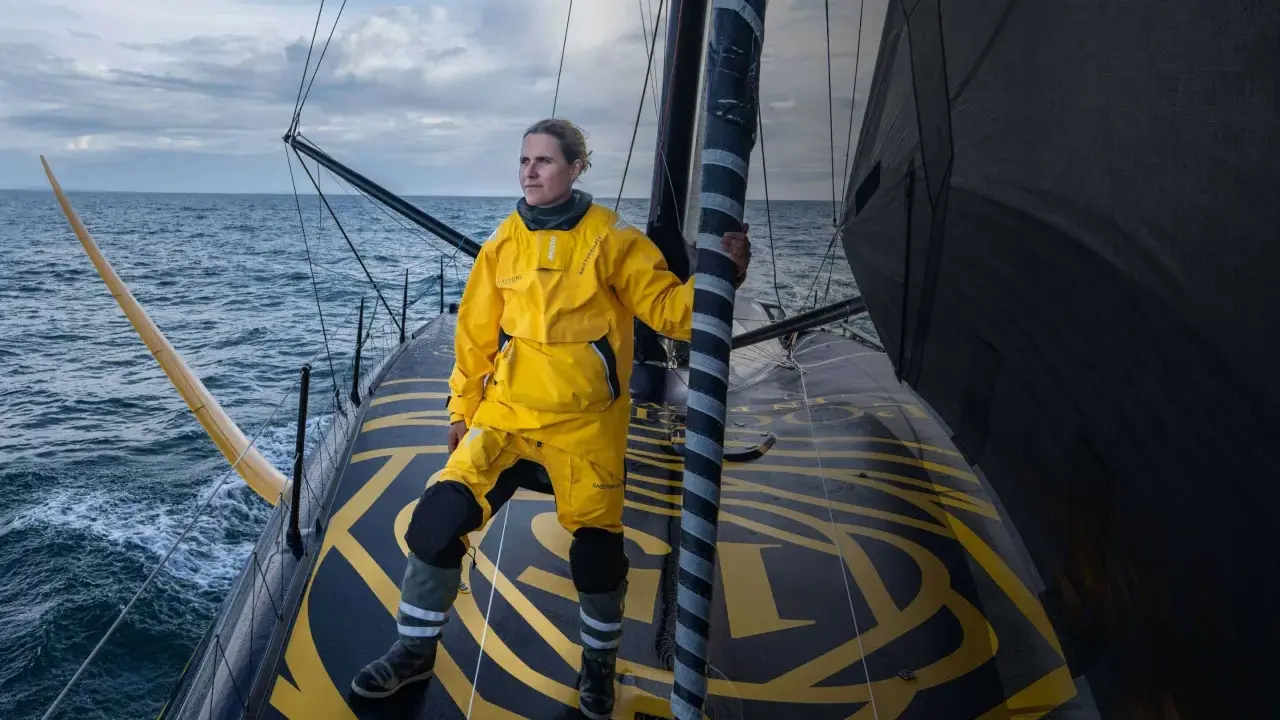 Clarisse Crémer, en tenue de voile jaune vif, se tient fièrement sur le pont d'un voilier, prête à affronter les éléments.
