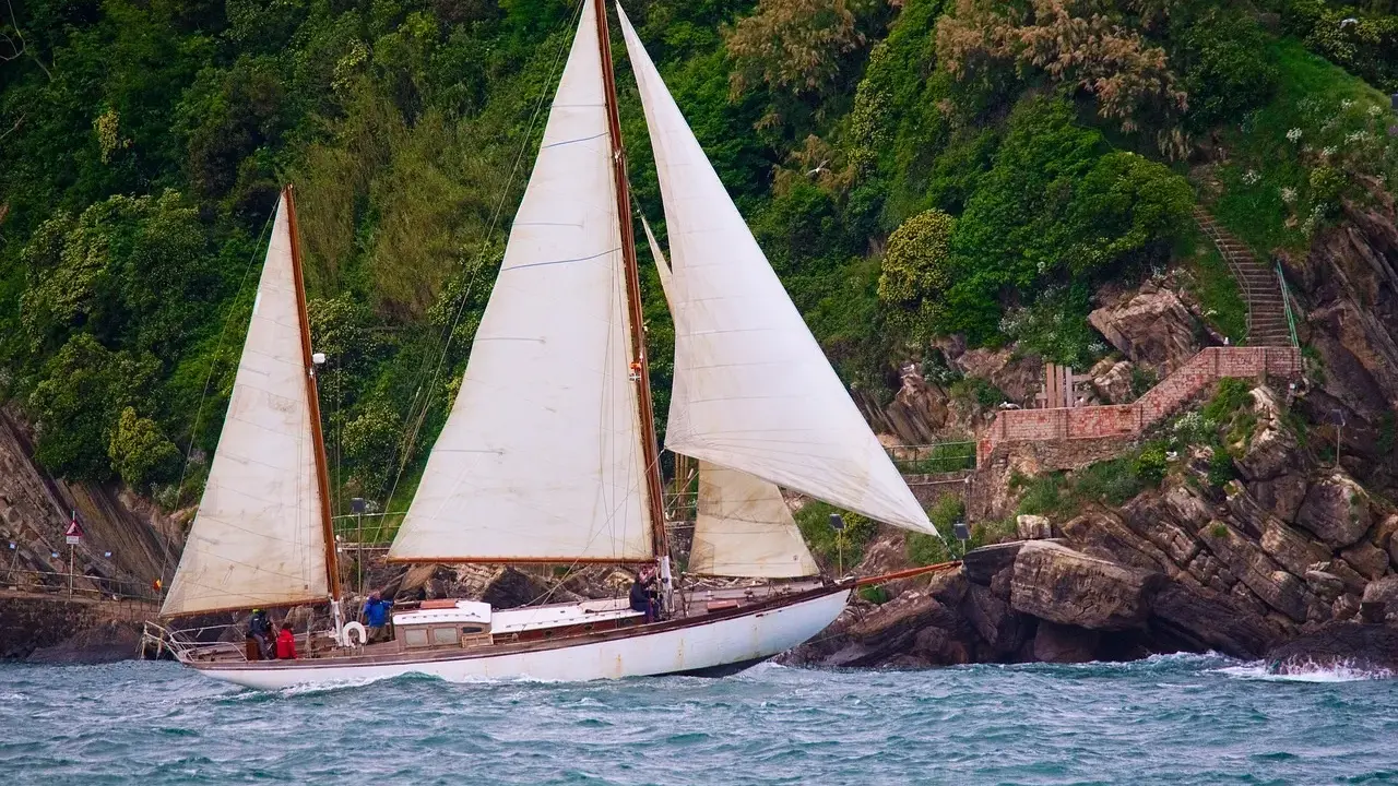 Un magnifique voilier 2 mâts navigue près d'une côte rocheuse verdoyante.