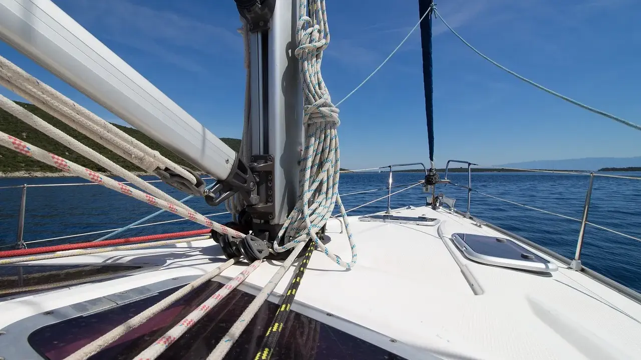 Vue de l'avant d'un voilier naviguant sur une mer bleue. Les cordages sont bien rangés, prêts à hisser le grand mât.