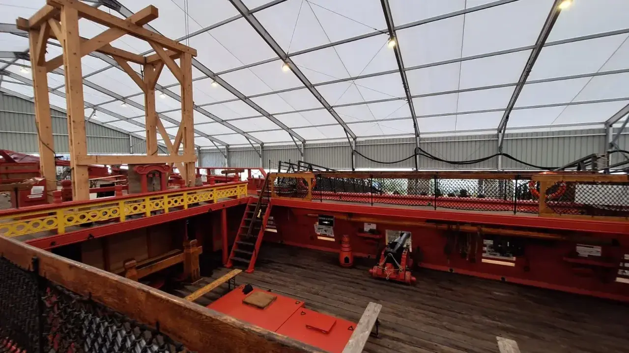 L'intérieur du **bateau Hermione** est en cours de restauration. On voit la structure en bois, les ponts rouges et jaunes, et un canon.