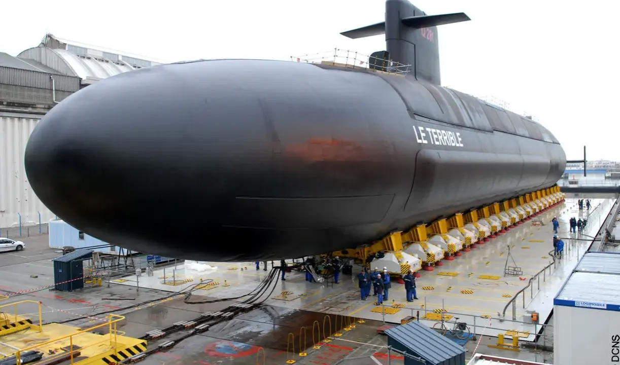 Le sous-marin "Le Terrible" est en cours de construction, sa taille impressionnante est mise en valeur sur des supports jaunes.