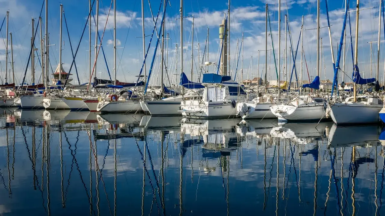 Une flotte de voiliers anglais, leurs mâts élancés se reflétant sur l'eau calme d'un port sous un ciel bleu éclatant.