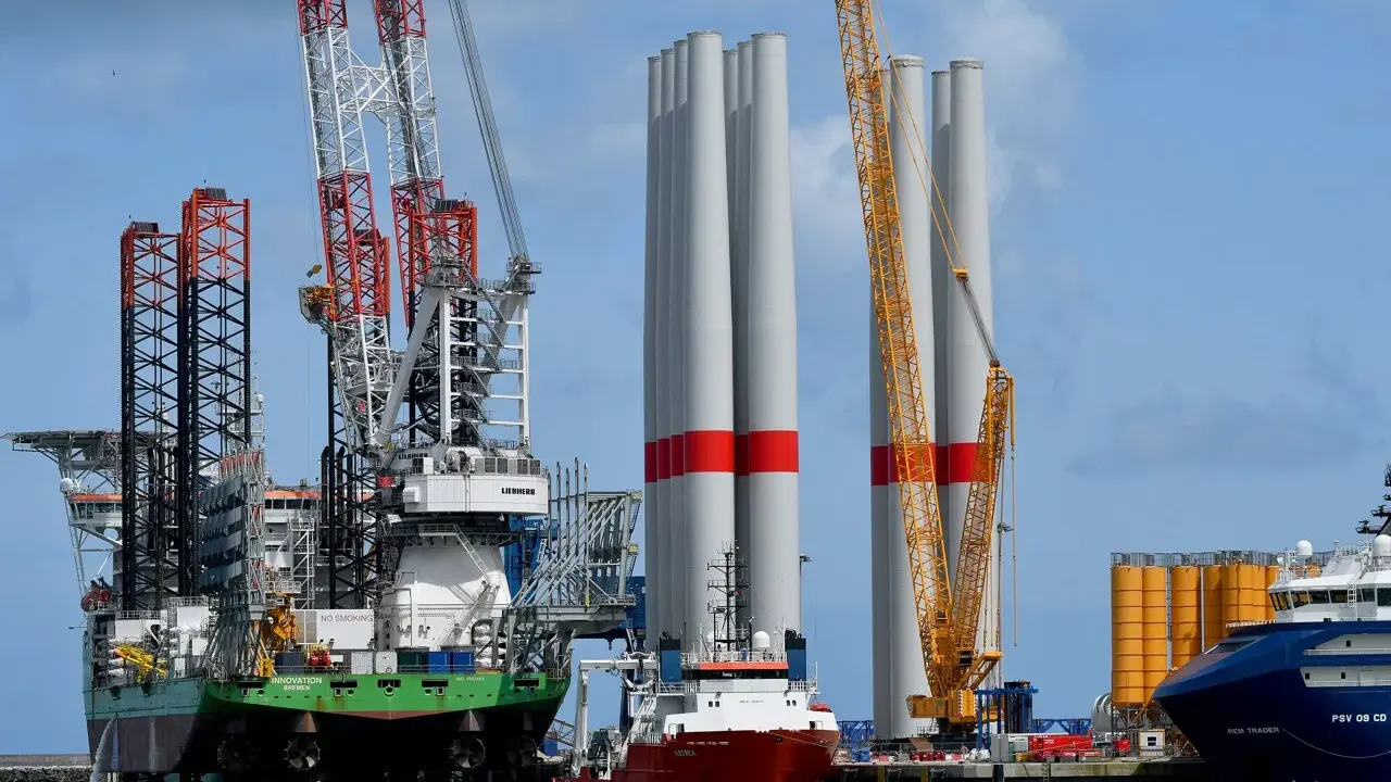 Un navire jack-up avec des grues massives se tient à côté de grandes tours d'éoliennes, prêt pour l'installation.