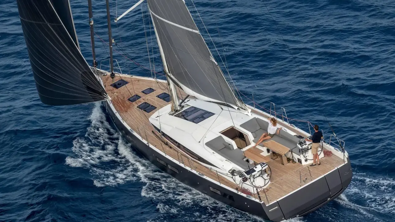 Un couple profite d'une croisière sur un voilier habitable à l'année, naviguant sur des eaux bleues par une journée ensoleillée.