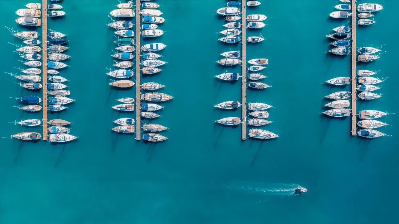 Vue aérienne d'un port où de nombreux voiliers sont amarrés. Un petit bateau navigue, laissant une trace dans l'eau. Le **bloc côtier obligatoire** est bien visible.