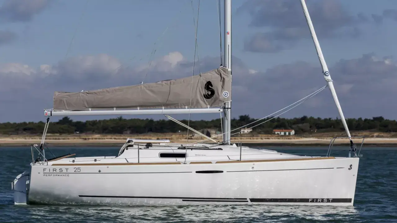 Voilier blanc "First 25 Performance" naviguant sur une mer calme, avec une voile grise arborant un logo noir.