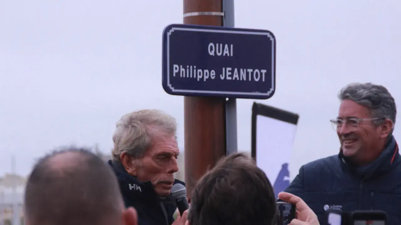 Un panneau "Quai Philippe JEANTOT" honore le navigateur. Philippe JEANTOT, entouré, parle au micro.