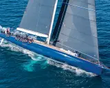 Un voilier bleu vif glisse sur l'eau, ses voiles sombres déployées comme un tapis volant 3. L'équipage est visible sur le pont.