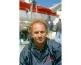 Jean-Claude Parisis, navigateur, souriant devant un avion rouge et blanc.