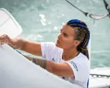 Marie Tabarly, concentrée, ajuste une voile sur son bateau. Ses tresses bleues et brunes flottent au vent.