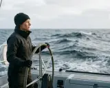 Une femme au gouvernail d'un bateau ardent, naviguant sur une mer agitée sous un ciel couvert.