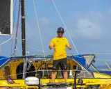 Arnaud Boissières, souriant, fait un double pouce levé sur son voilier jaune et bleu, prêt pour une nouvelle aventure en mer.
