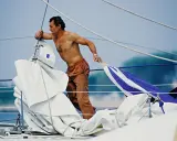 Un marinier, peut-être Eric Tabarly, manipule des voiles sur un bateau. Sa fortune est dans le vent et l'océan.