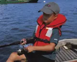 Un enfant pêche en mer, portant un gilet de sauvetage obligatoire. La question du gilet de sauvetage obligatoire jusqu'à quel âge est cruciale pour la sécurité nautique.