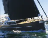 Un voilier moderne, avec une grande voile noire, navigue sur une mer agitée. Xavier Desmarest admire la vue depuis le pont.