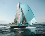 Un voilier de course, le numéro 1068, navigue sur une mer agitée. Les voiles, l'une noire et l'autre bleu clair, portent le nom "la maison perchée". Thais Le Cam est à la barre.
