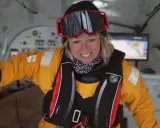 Alexia Barrier, souriante, porte une combinaison jaune et un gilet de sauvetage, prête pour une aventure maritime.