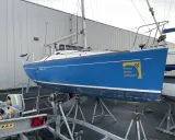 Voilier bleu FIRST 210 sur bers, prêt pour la saison. Le logo "Presse Matin Diffusion" est visible sur la coque.