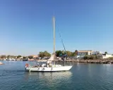 Un voilier atlante navigue sur des eaux calmes, avec des personnes à bord. Le ciel est bleu et dégagé.