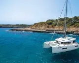 Un catamaran blanc, le "StarElli", navigue dans des eaux turquoise près d'une côte rocheuse et verdoyante. Ce safran catamaran offre une vue idyllique.
