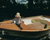 Un enfant en chapeau fleuri explore l'intérieur d'un bateau en bois, le Morgat 320, prêt pour l'aventure.