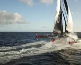 Le trimaran "Actual" d'Yves Le Blevec fend les vagues, propulsé par le vent sous un ciel bleu.