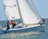 Équipage concentré sur un foc voilier blanc, naviguant sur une mer agitée sous un ciel bleu clair.