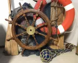 Roue de gouvernail en bois, filet de pêche, bouée de sauvetage orange et pagaies évoquent un safran de bateau prêt pour l'aventure.