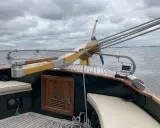 Installation pilote automatique barre franche sur un voilier, avec drapeau néerlandais et ciel couvert.