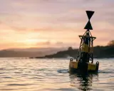 Une bouée jaune et noire, un bms bateau, flotte sur l'eau calme au coucher du soleil.
