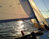 Voile d'un bateau au coucher du soleil, reflets dorés sur l'eau. La balancine du bateau est bien tendue.