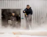 Deux hommes utilisent un nettoyeur haute pression pour nettoyer un voile de bateau avec du savon noir.
