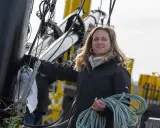 Élodie Bonafous, souriante, tient une corde bleue sur un bateau, entourée de cordages et de structures métalliques.