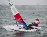 Jeune navigatrice en dériveur **tabur 320**, voile rouge et bleue, naviguant sur une mer agitée.
