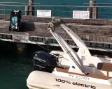 Un bateau électrique est prêt à être rechargé sur un ponton en bois. Une borne de recharge AQUA est visible à proximité.