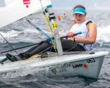 Jeune femme concentrée naviguant en deriveur solo, le bateau #063 fend les vagues.