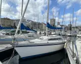 Un voilier blanc aux voiles bleues, amarré dans un port. L'avis sur ce voilier rush est qu'il est prêt pour la prochaine aventure.