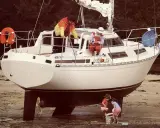 Le voilier "Évasion 29" échoué sur la plage, avec deux enfants jouant à ses pieds et deux adultes à bord.
