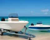 Deux bateaux blancs sur une plage de sable fin, l'un sur une remorque. Idéal pour un compromis vente bateau sous le soleil.