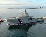 Un imposant bateau garde côte, le Landhelgisgæslan, navigue en mer, escorté par un remorqueur et suivi par des canots. Un hélicoptère survole la scène.