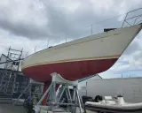 Le nouveau bateau de Jean Le Cam, un voilier blanc et rouge, est sur des supports à côté d'un atelier.