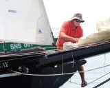 Un homme, Guy Bernardin, ajuste les voiles du Spray, un voilier historique, par une journée ensoleillée.