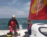 Franck-Yves Escoffier et un jeune garçon naviguent sur un voilier par temps ensoleillé.
