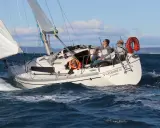 Un bateau symphonie navigue sur des eaux bleues, trois personnes à bord profitent du soleil.